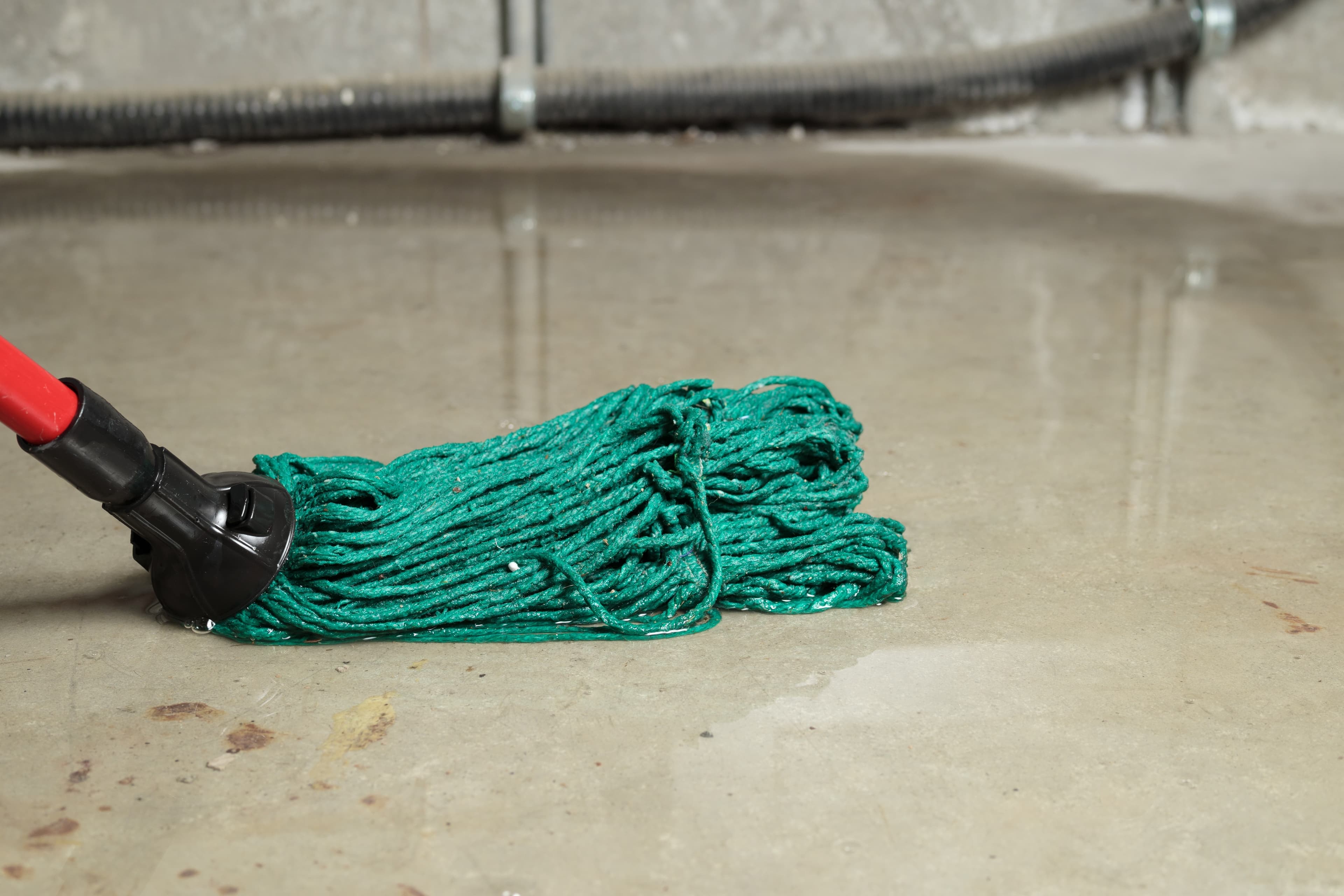 Green mop on wet basement floor near pipes.