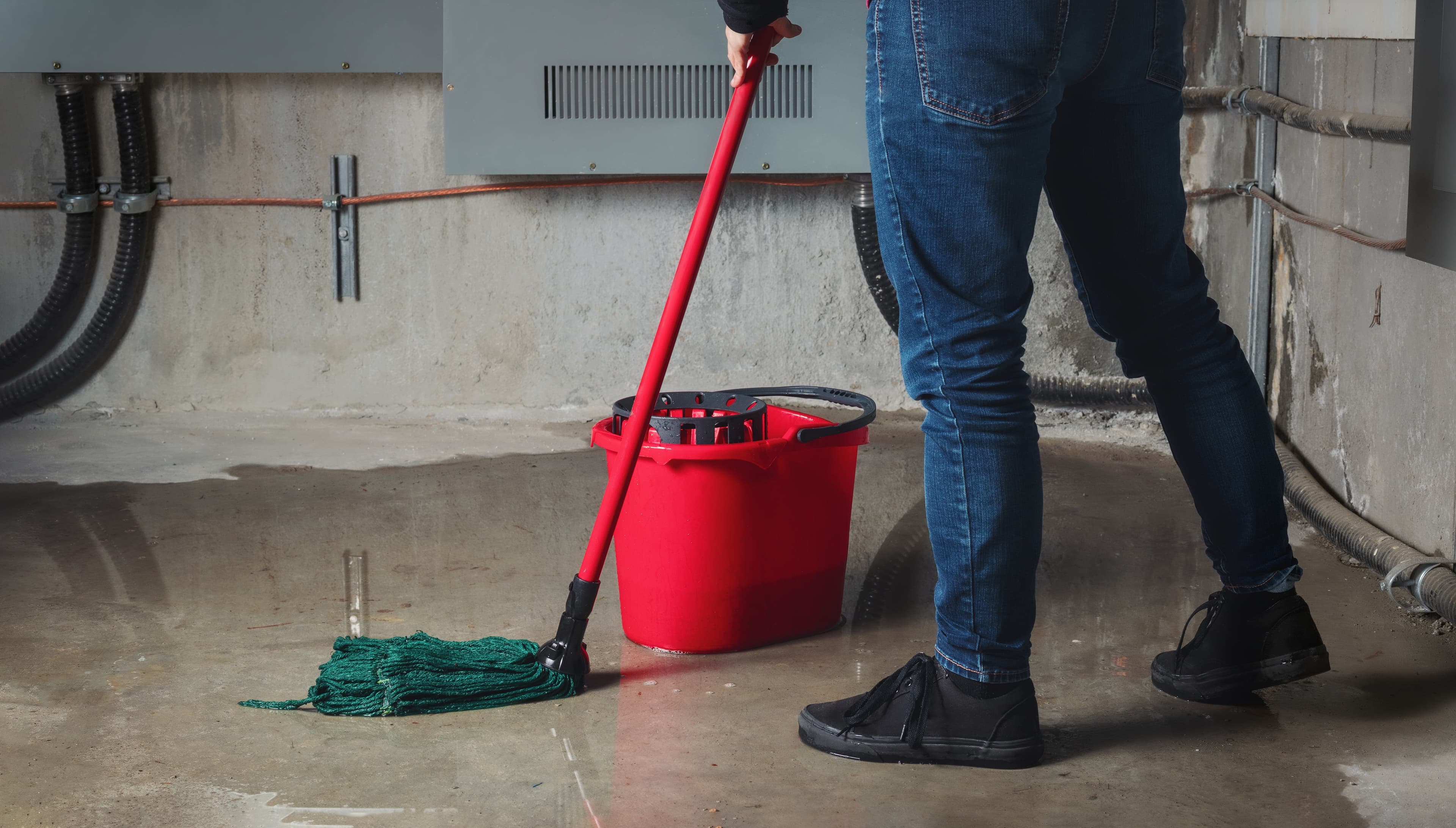Person mopping wet basement floor with red bucket.