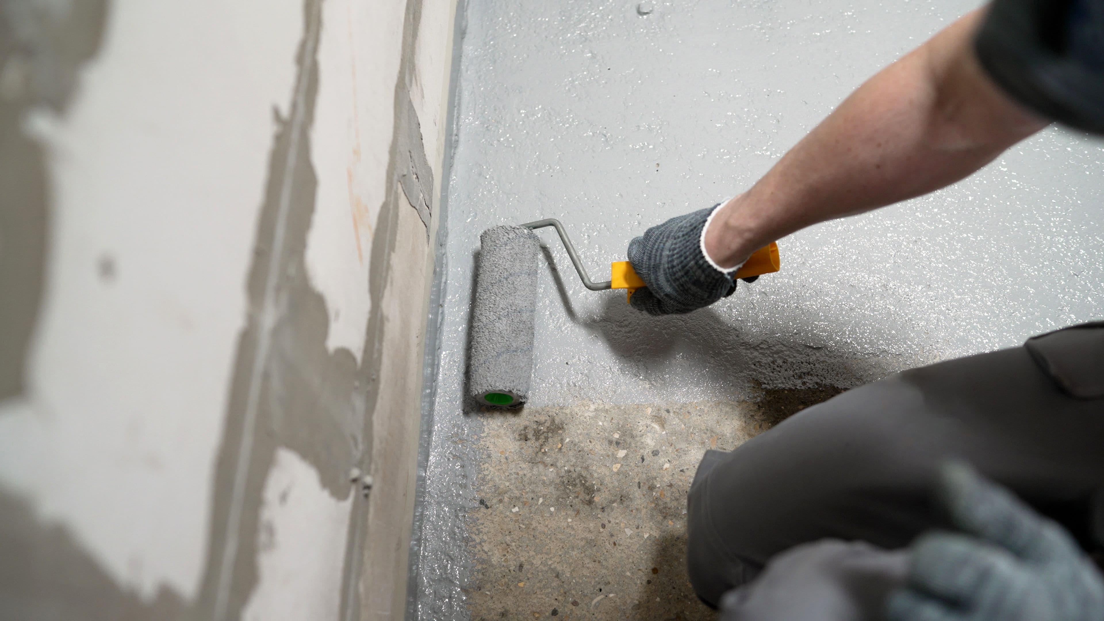 Person applying waterproof coating to basement floor with a roller.