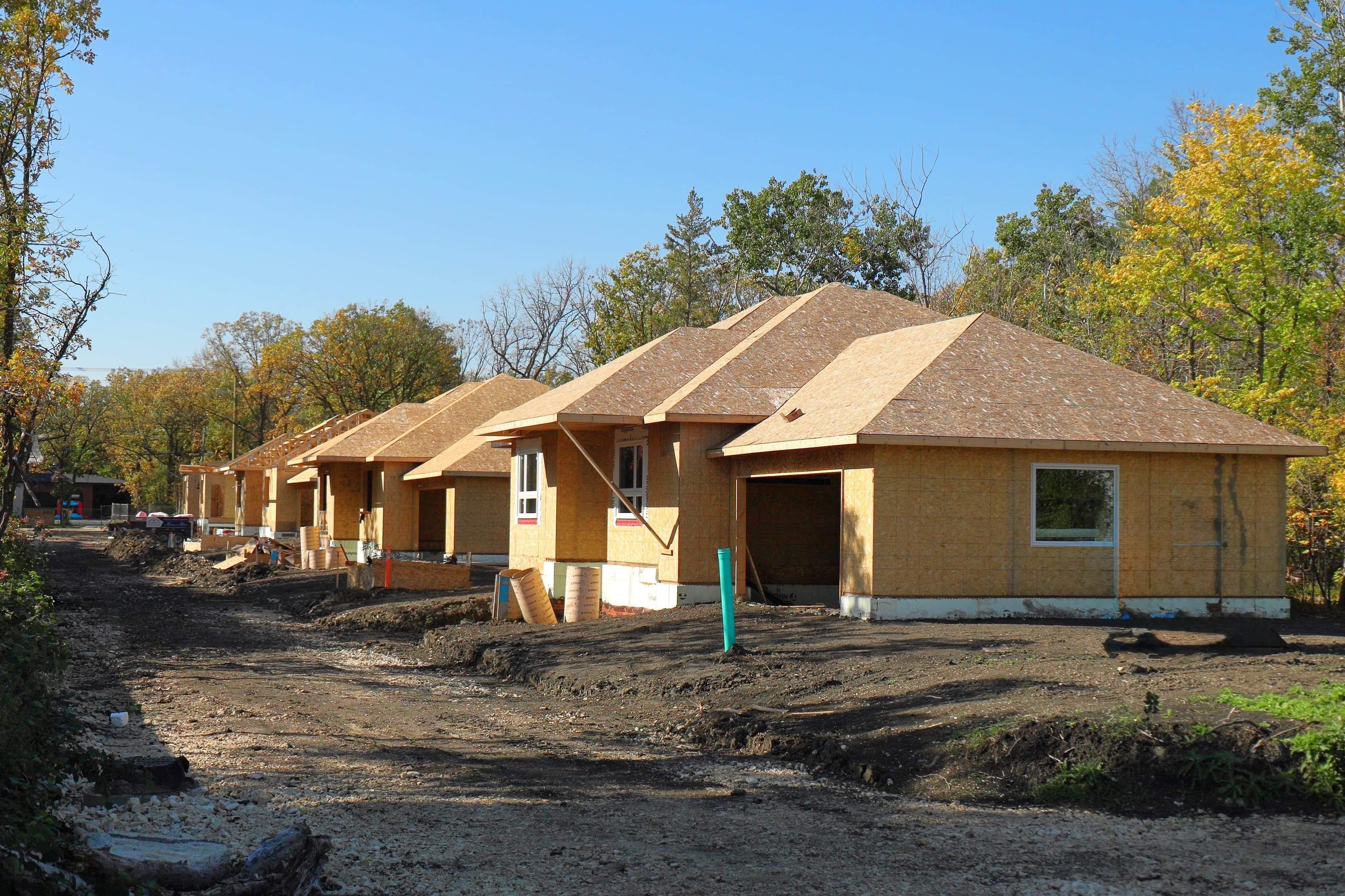 Row of homes under construction in wooded area with autumn foliage.
