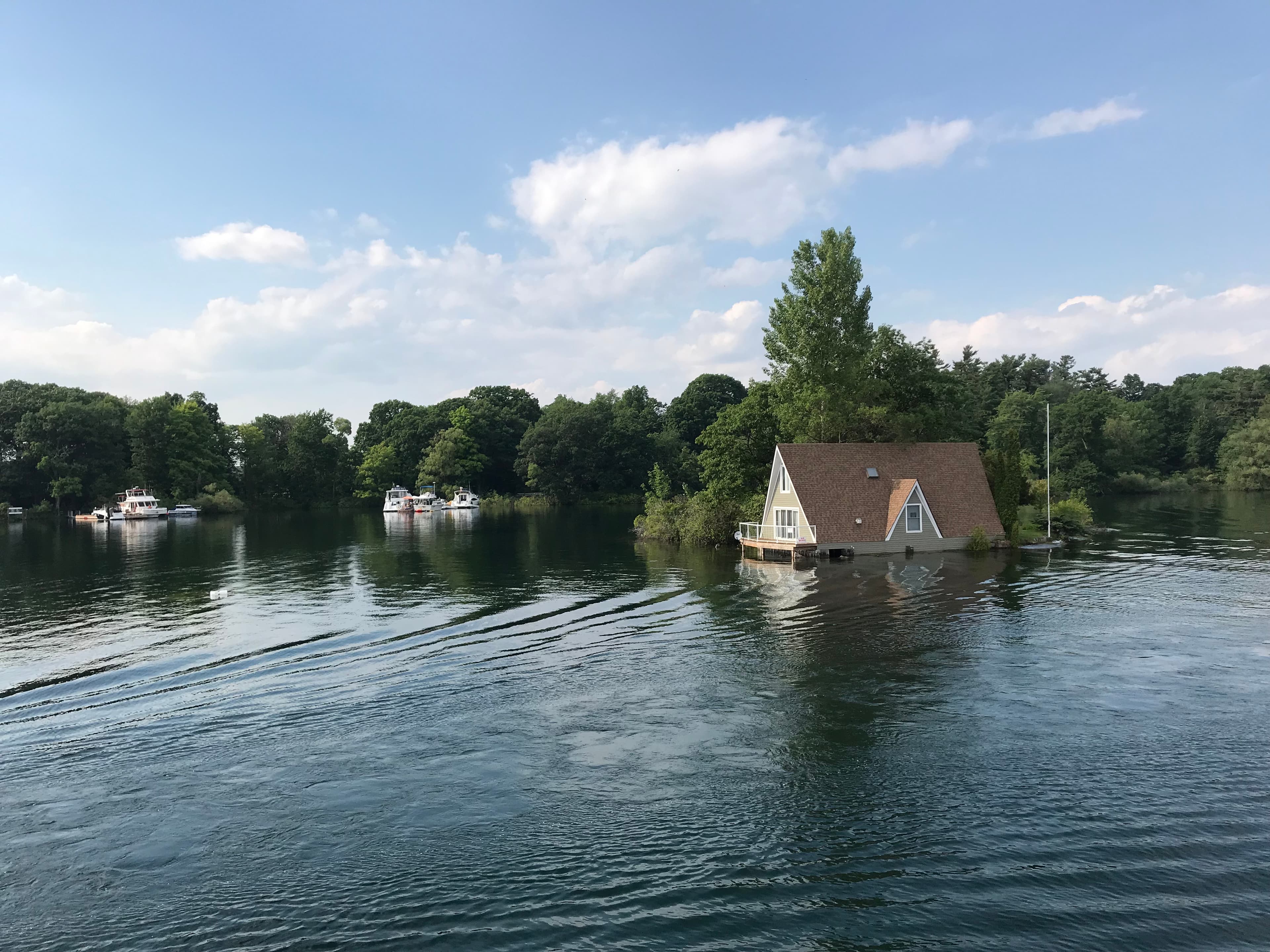 Submerged A-frame house surrounded by floodwaters and trees.