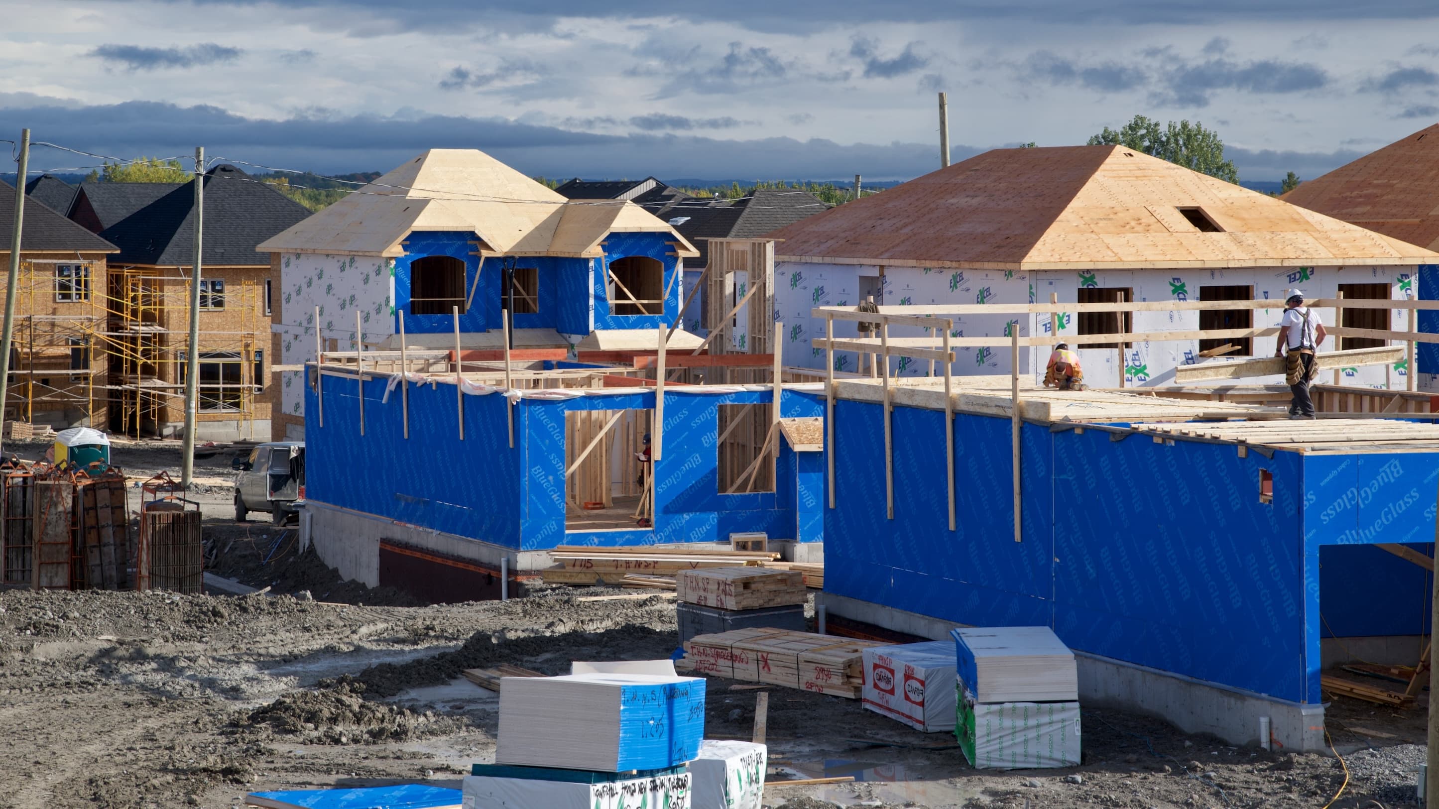 Construction site with workers and houses in progress under cloudy sky.